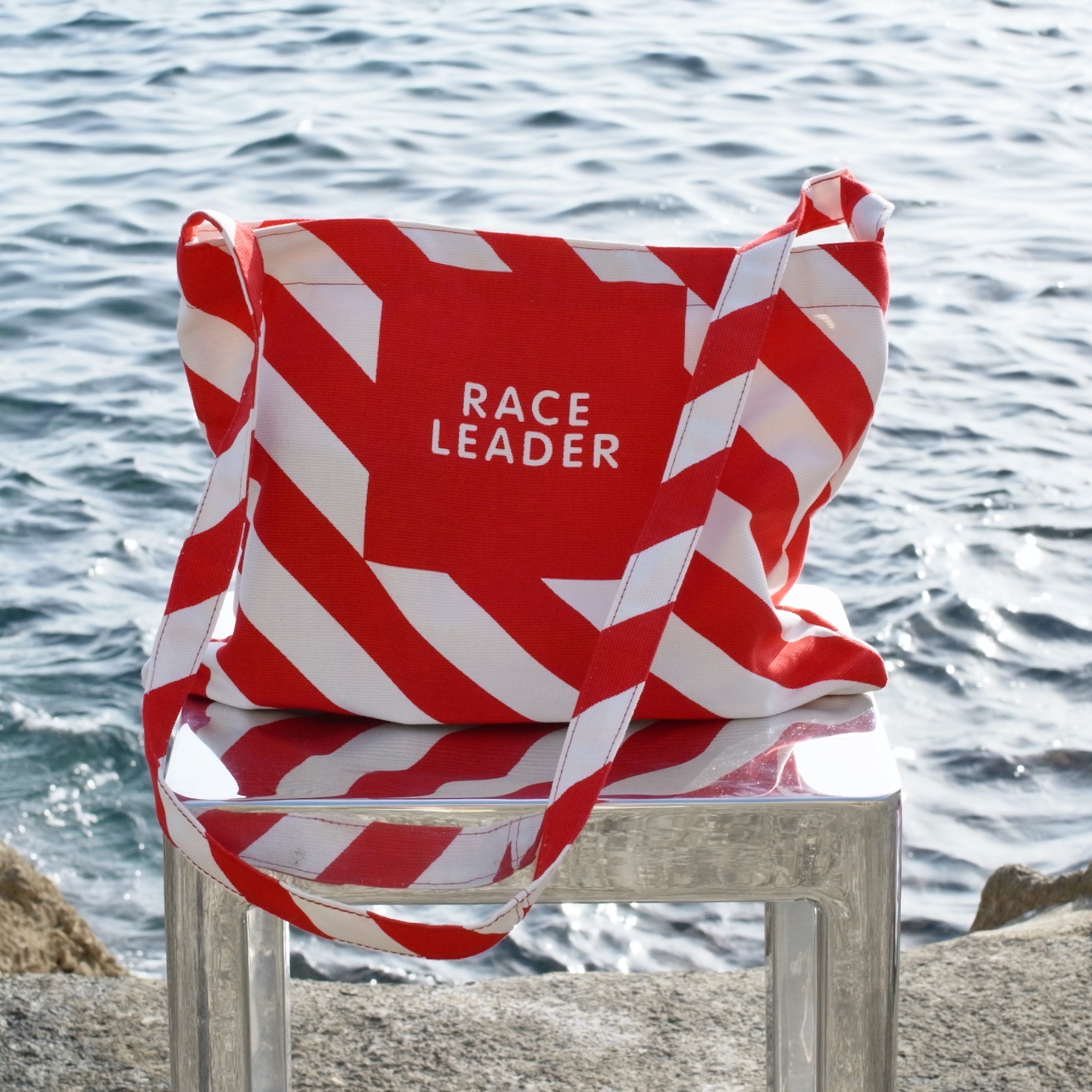 Red and white striped shoulder-bag with 'RACE LEADER' text on a chair by the water.