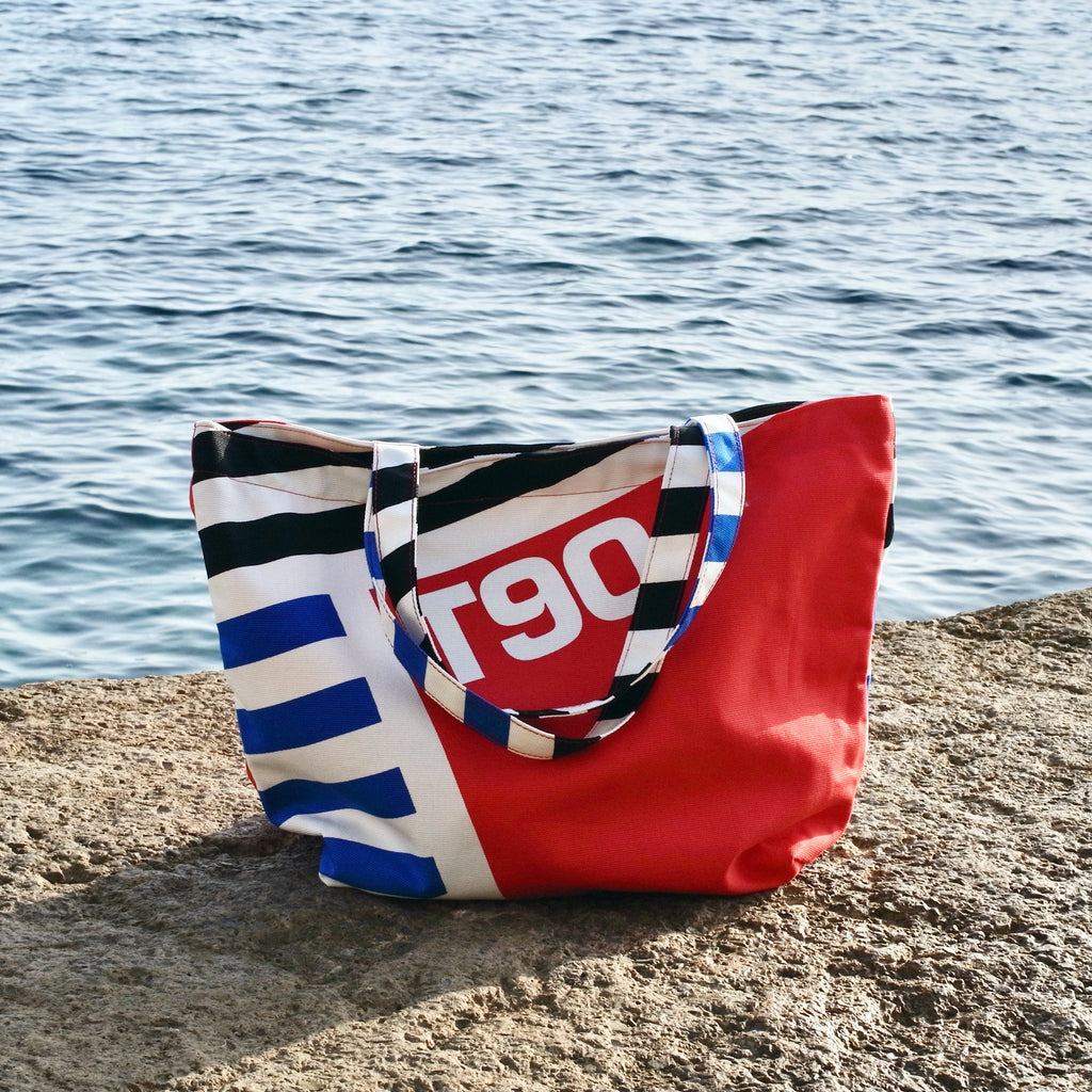 Red and black striped bag with 'T90' design on a concrete ledge by a body of water.