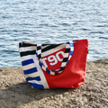 Red and black striped bag with 'T90' design on a concrete ledge by a body of water.