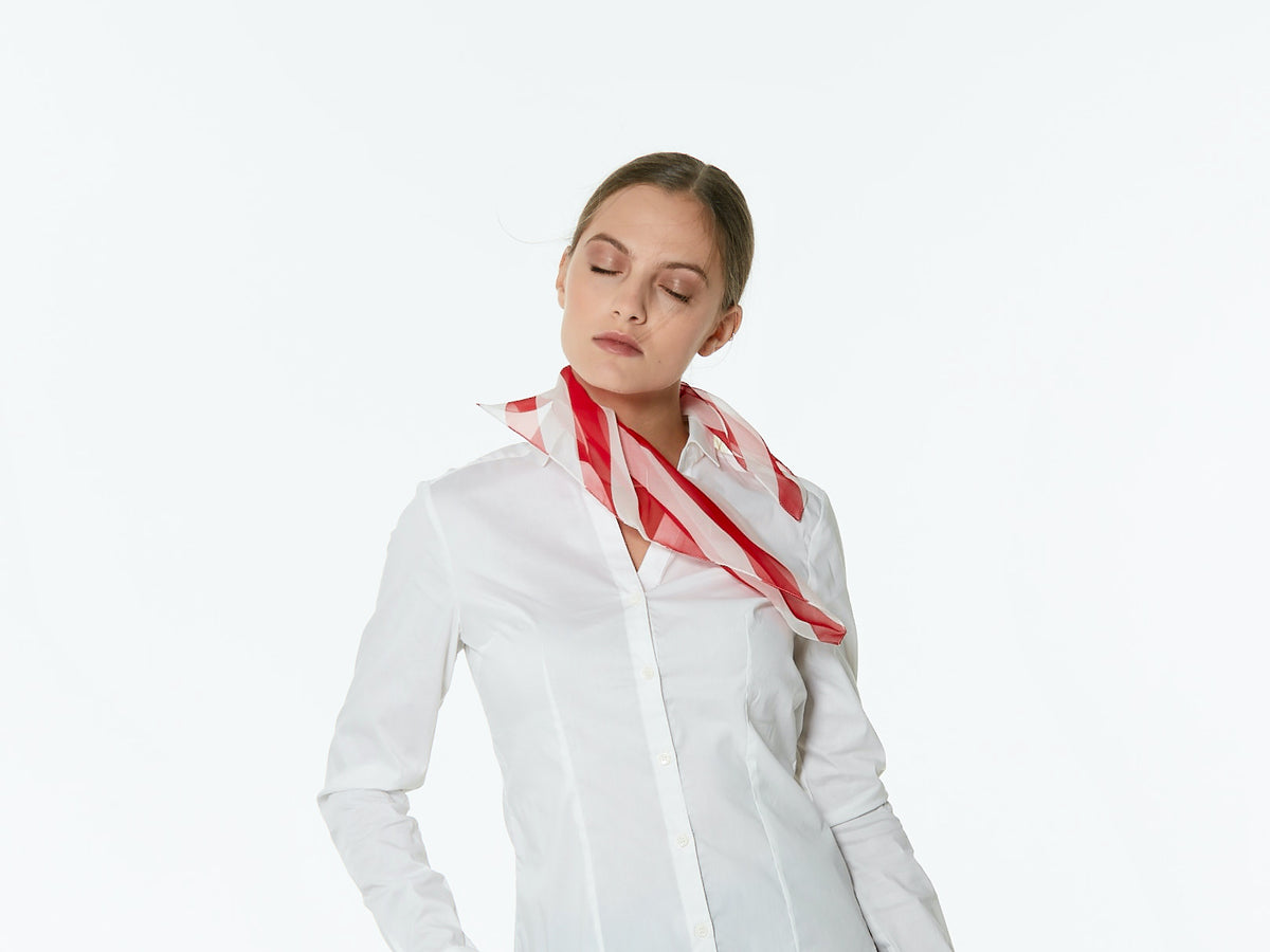 A woman wearing a white button-up shirt and a red and white striped Superleggero silk scarf, posed against a solid white studio background.