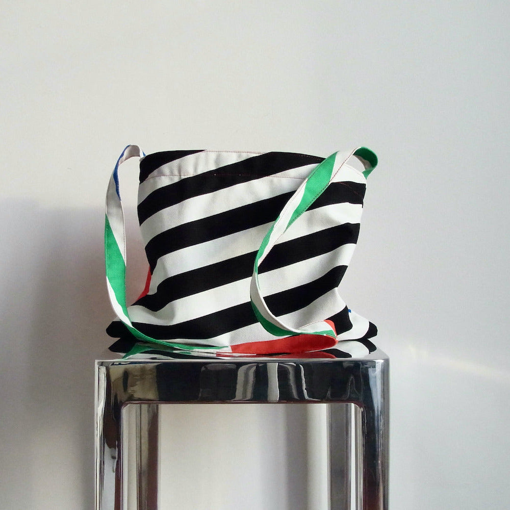 Striped bag with green and red accents on a metallic stand against a white background