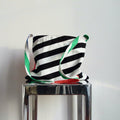 Striped bag with green and red accents on a metallic stand against a white background
